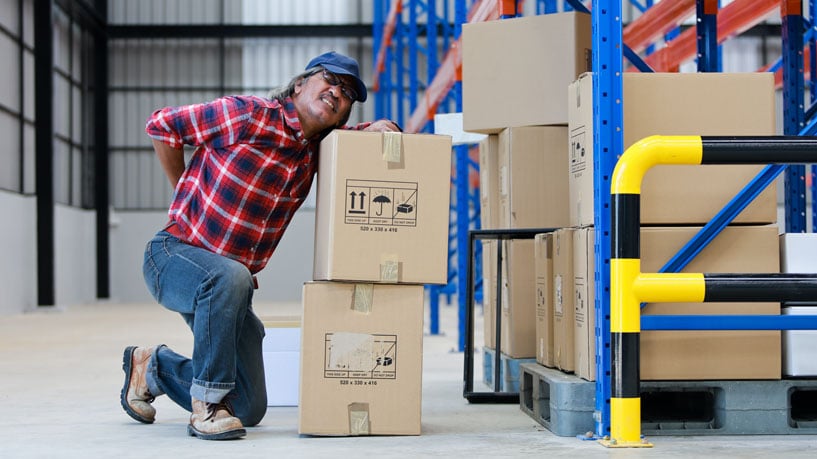 A man lifting heavy boxes reaches for his back after an apparent spine injury.