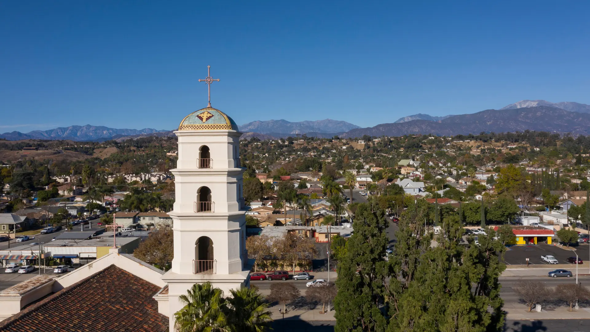 Bell tower with mountains and suburban neighborhood under a clear blue sky.