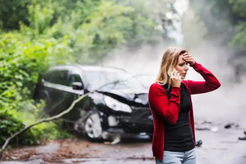 Woman on phone after car crash on a foggy road.