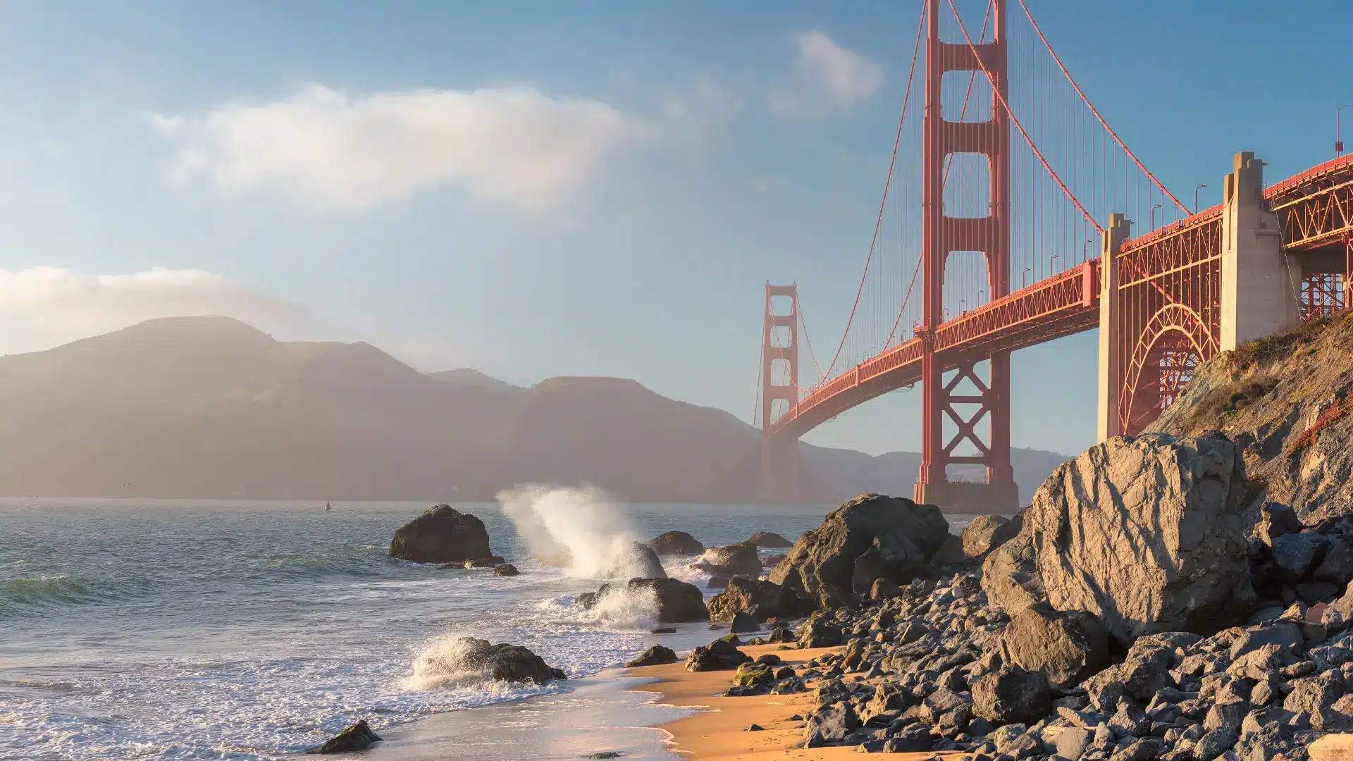 View of the Golden Gate Bridge from the beach, showcasing its iconic towers against a clear blue sky.