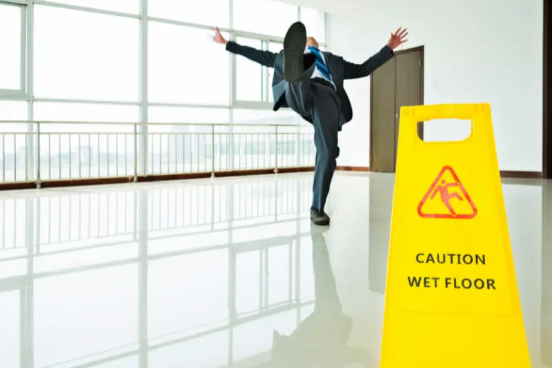 Illustration of a person slipping on a wet floor with a caution sign, representing a California slip-and-fall accident guide, legal steps to take, and factors affecting injury claim value.