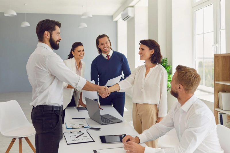 Business professionals shaking hands in an office setting, symbolizing agreement and collaboration.