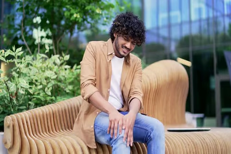 A man experiencing knee pain while seated on a bench outdoors.